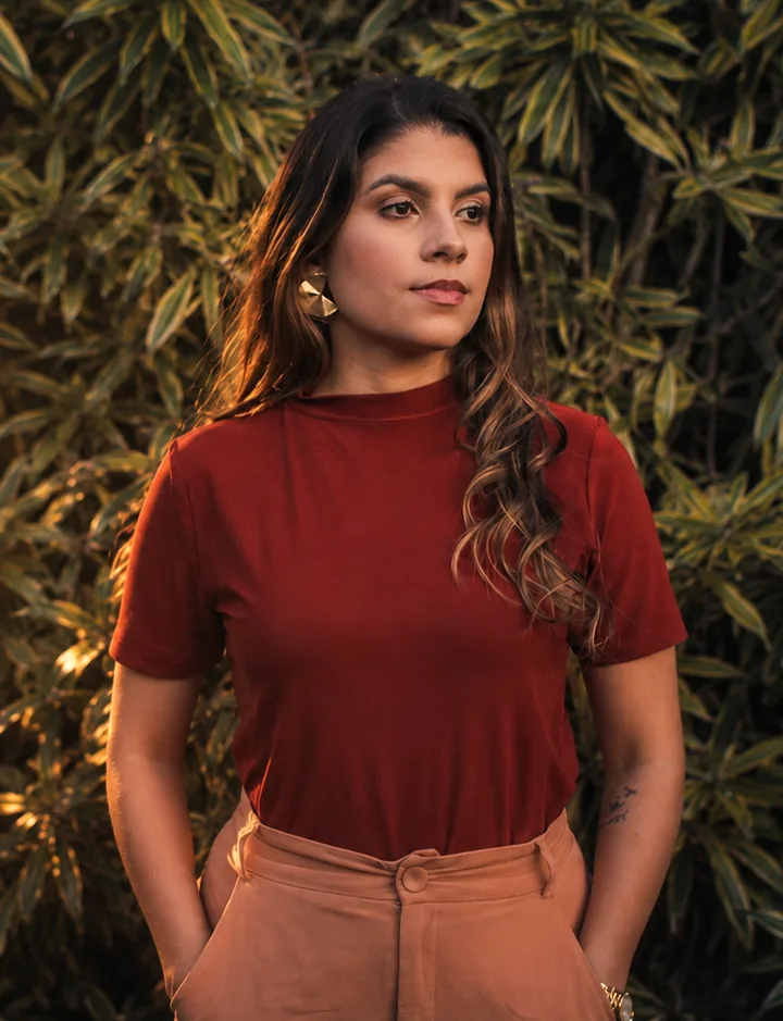 Natalie Cavalcante ao ar livre, entre folhagens, na luz dourada do fim de tarde.